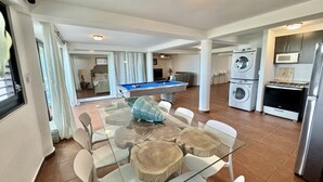 A spacious living area with a glass-top dining table surrounded by white chairs, a pool table, and a kitchen area with a stove, microwave, and washing machine. - Endless ocean views and pool, by El Yunque. (Río Grande)