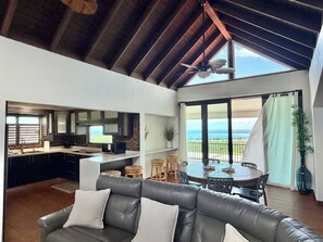 A modern kitchen with a view of the ocean, a dining area with a table and chairs, and a living room with a leather sofa. - Endless ocean views and pool, by El Yunque. (Río Grande)