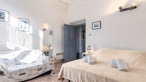 Een slaapkamer met een bed, een nachtkastje met een lamp, een wandlamp en een deur naar een andere kamer.