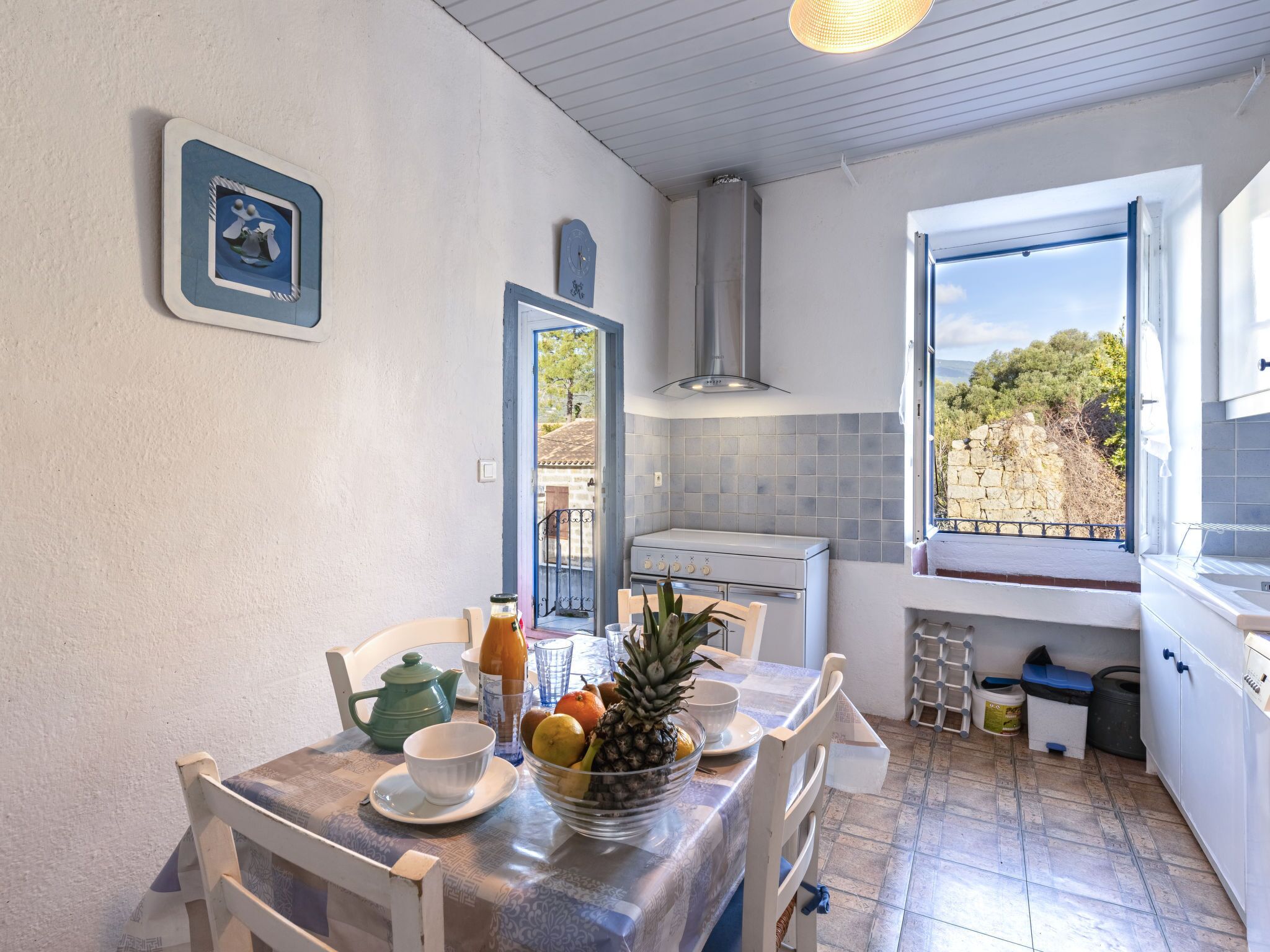 A compact kitchen with a dining area, featuring a stove, sink, and window with a view of greenery.