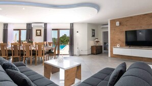Un salon moderne avec un coin repas, une vue sur la piscine et un téléviseur à écran plat.