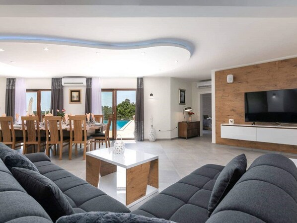 A modern living room with a dining area, a pool view, and a flat-screen TV.