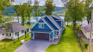 A two-story house with a dark blue exterior, a garage, and a well-maintained lawn. - Blue Skies - Lakefront Living at it's Finest! Luxury Amenities! (Honeoye)