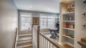 A staircase leading to a dining area with a table and chairs, a bookshelf with books, and a window with a view of the outside. - Blue Skies - Lakefront Living at it's Finest! Luxury Amenities! (Honeoye)