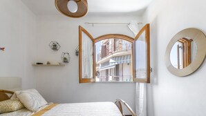 A bedroom with a large bed, a window with an open curtain, a mirror, and a shelf with decorative items. - Apartment Atena by Interhome (Giardini Naxos)