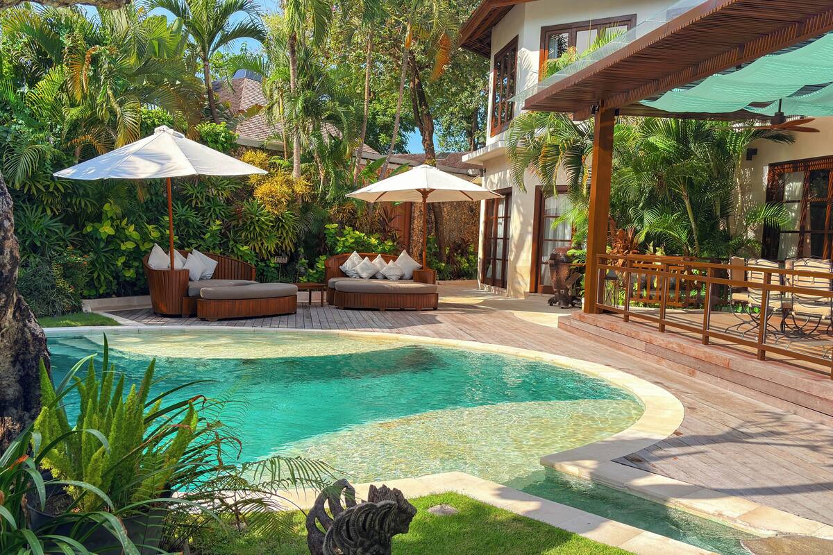 A pool area with a wooden deck, lounge chairs, and umbrellas.