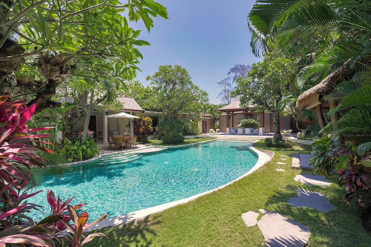A swimming pool surrounded by lush greenery and thatched-roof structures.