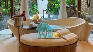 Un área de spa con una bañera grande, un taburete de madera y un recipiente de vidrio con una toalla.