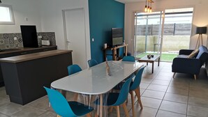 Une cuisine moderne avec un îlot central, un coin repas avec des chaises bleues et un espace de vie comprenant un canapé et un téléviseur.