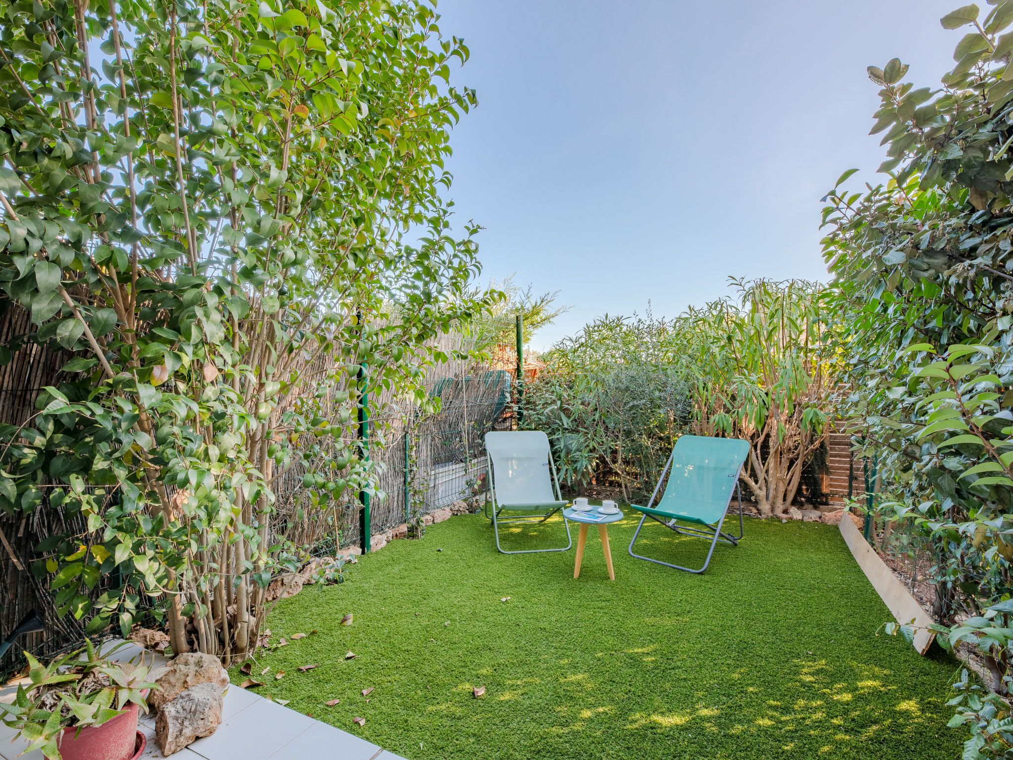 A garden with two green chairs, a small table, and a potted plant.