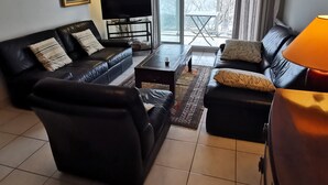 A living room with a black leather sofa, a coffee table, and a TV on a stand. - The Dunes of Blossac 100m from the beach (Les Sables-d´Olonne)