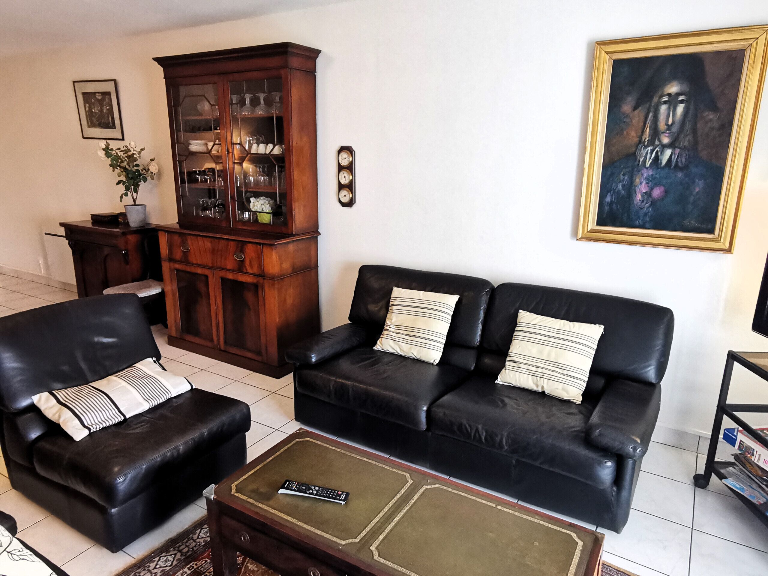 Ein Wohnzimmer mit einem schwarzen Ledersofa, einem passenden Sessel, einem Couchtisch, einem Holzschrank und einem Bild an der Wand.