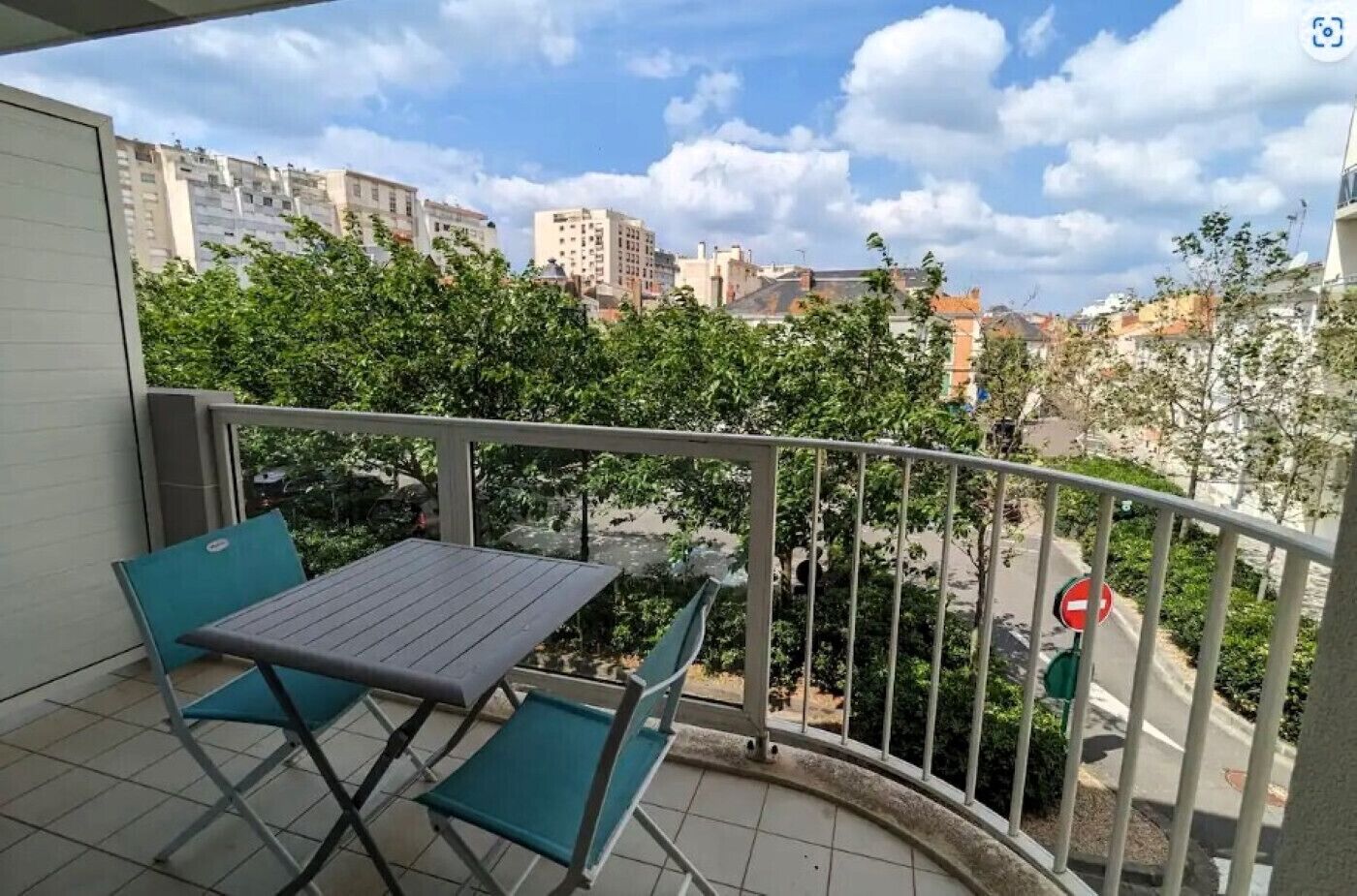 A balcony with a table and chairs, overlooking a cityscape with buildings and trees.