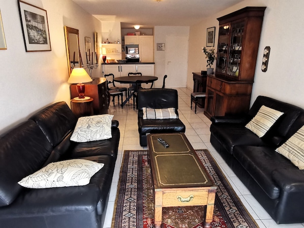 A living room with two black leather sofas, a wooden coffee table, and a dining area with a table and chairs.
