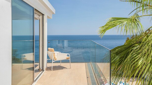 Un balcón con puerta de cristal, una silla blanca y vista al océano.