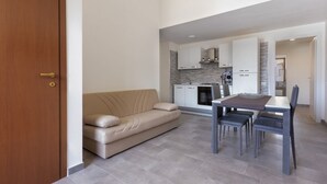 Un salon moderne avec un canapé, une table à manger, des chaises et une cuisine en arrière-plan.
