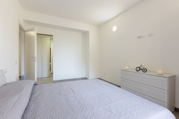 A bedroom with a bed, a dresser, and a door leading to another room.