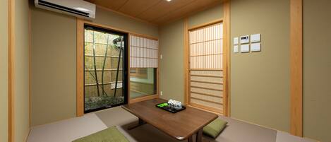 Ein traditioneller japanischer Raum mit Tatami-Boden, einem niedrigen Holztisch, Schiebetüren und Blick auf einen Bambuszaun.