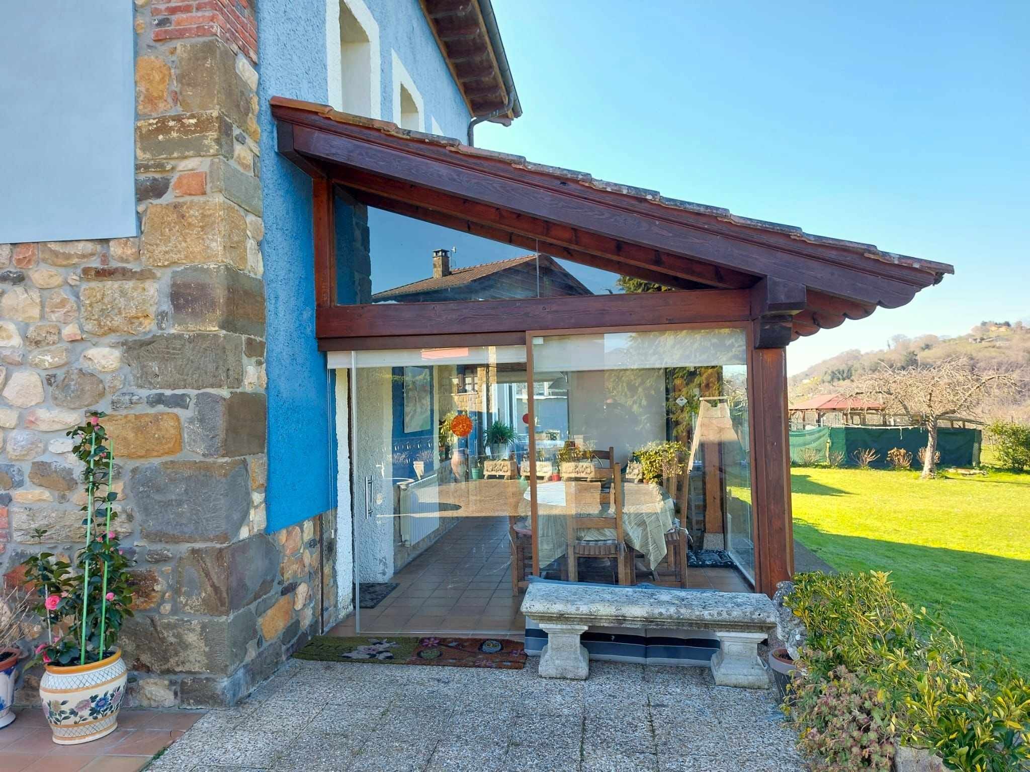 Un edificio de piedra con entrada de vidrio, una pérgola de madera y un banco en el exterior.