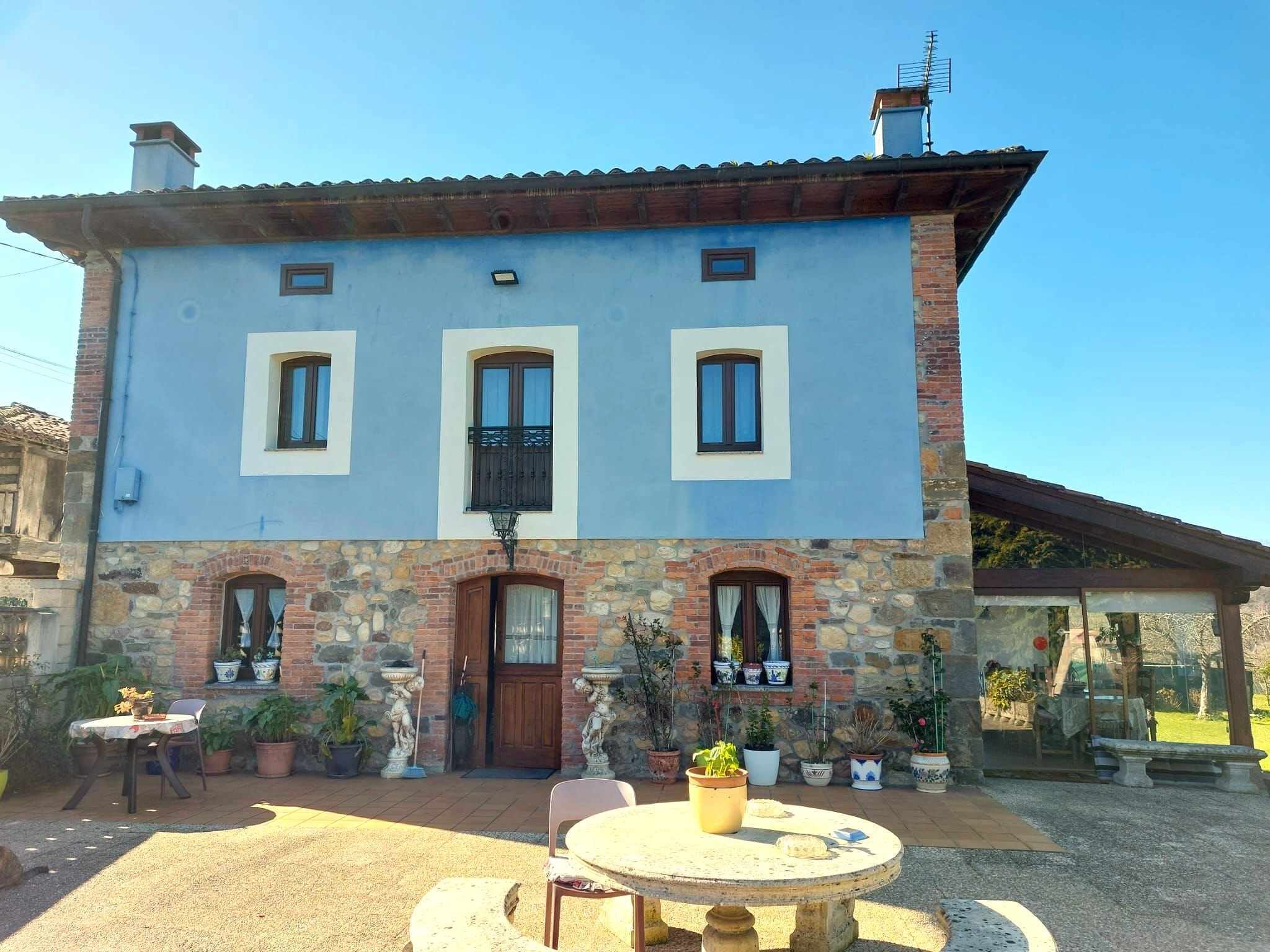 Un edificio de dos pisos con fachada de piedra, una entrada central y un patio con mesa y sillas.