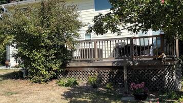 A house with a wooden deck, a fenced yard, and a small garden with pink flowers.