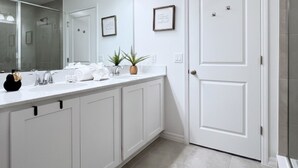 Een badkamer met een wit wastafelmeubel, een spiegel, een wastafel en een deur.