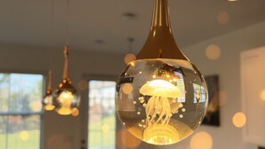 Een eethoek met een ronde tafel en stoelen, een hangende lamp met een glazen kap, en een plafondlamp.