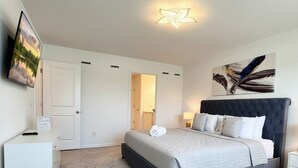 Een slaapkamer met een bed, nachtkastjes, een bureau, een deur en een kunstwerk aan de muur.