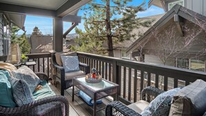 A covered outdoor seating area with wicker furniture, a glass table, and a view of neighboring houses and trees.