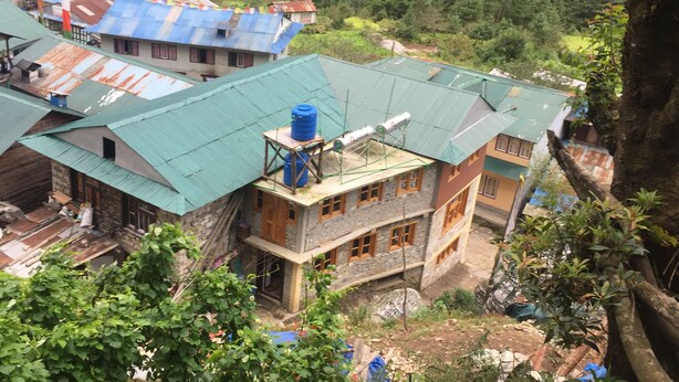 A multi-story building with a green roof, surrounded by lush greenery and a forested area. - Tribeni Lodge Restaurant And Bar (Phakding)