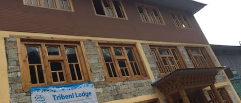 A multi-story building with wooden window frames and a sign for Tribeni Lodge.
