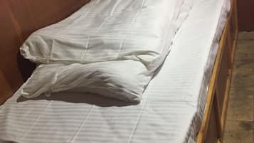A single bed with white bedding in a room with wooden walls and a patterned curtain.