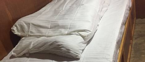 A single bed with white bedding in a room with wooden walls and a patterned curtain.