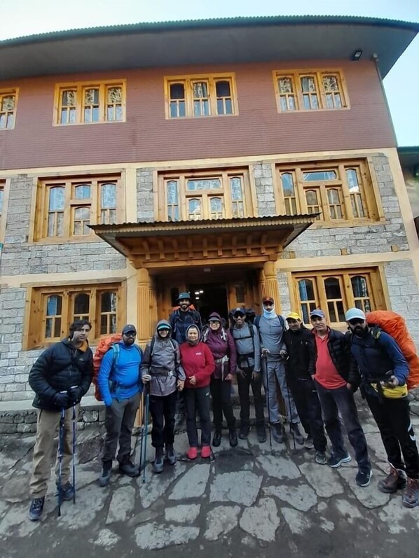 Un grupo de personas de pie frente a un edificio con muros de piedra y ventanas de madera.