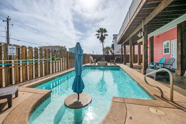A swimming pool with a wooden fence, lounge chairs, and a covered umbrella. - Corral Cottage- Private Pool Oasis, Games, Pets, Golf Cart zoned & Walk to Beach (Port Aransas)