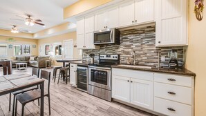 A modern kitchen with white cabinets, stainless steel appliances, and a tiled backsplash. - Corral Cottage- Private Pool Oasis, Games, Pets, Golf Cart zoned & Walk to Beach (Port Aransas)