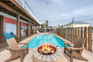 An outdoor pool area with Adirondack chairs, a fire pit, and a covered deck. - Corral Cottage- Private Pool Oasis, Games, Pets, Golf Cart zoned & Walk to Beach (Port Aransas)