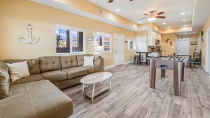 A spacious living room with a sofa, coffee table, and a foosball table. - Corral Cottage- Private Pool Oasis, Games, Pets, Golf Cart zoned & Walk to Beach (Port Aransas)