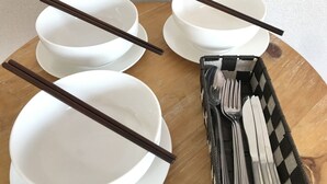A wooden table with four white bowls and chopsticks, and a napkin holder with utensils. - Best room in Kawagoe (Kawagoe)