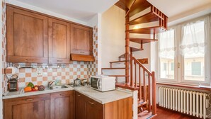 A kitchen with wooden cabinets, a microwave, a sink, and a staircase leading to a balcony. - La Torre In The Center Of Town, Sauze d'Oulx, Italy (Sauze d'Oulx)