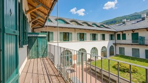 A building with a wooden balcony, green shutters, and a courtyard with a view of a mountain. - La Torre In The Center Of Town, Sauze d'Oulx, Italy (Sauze d'Oulx)
