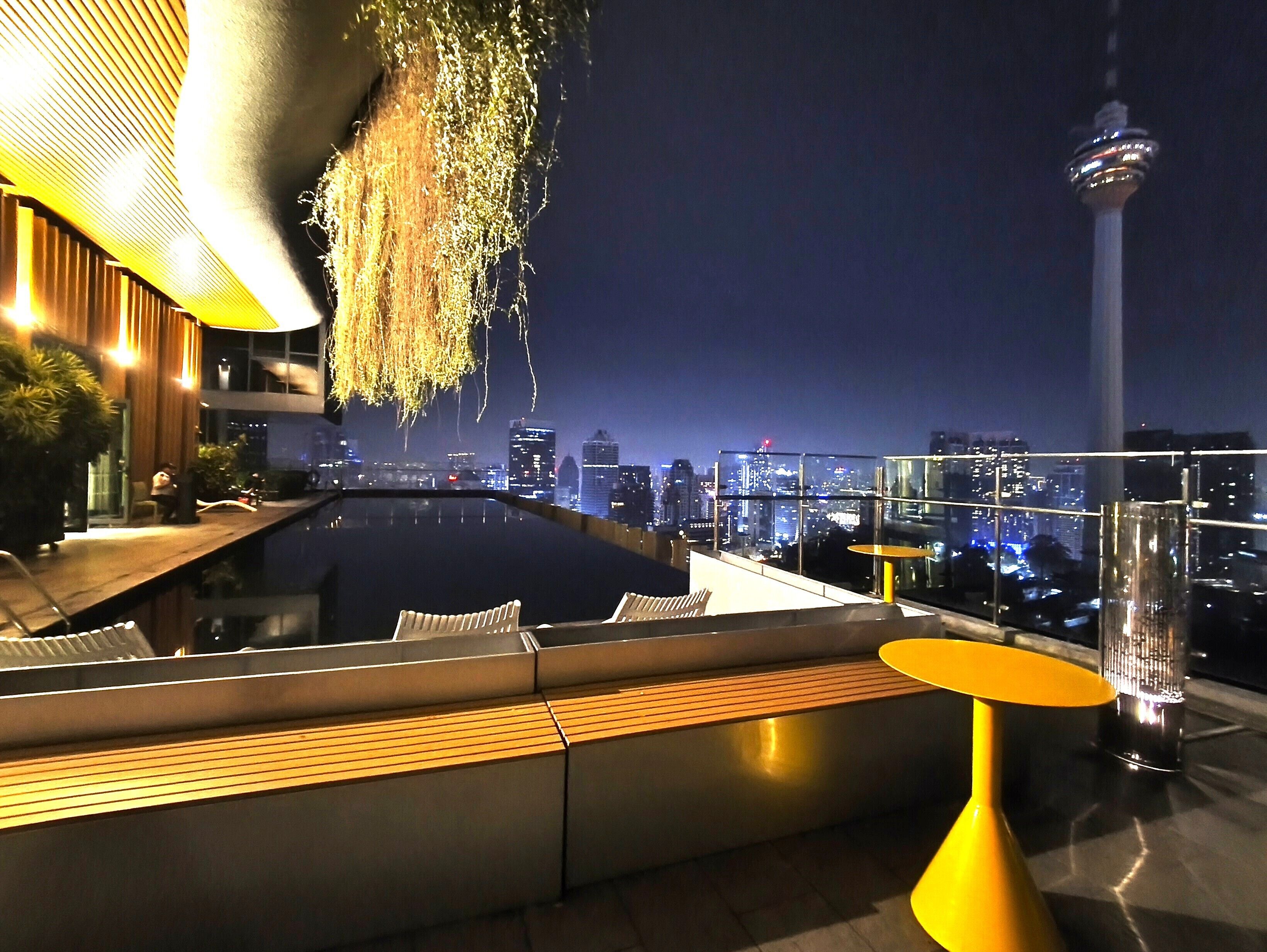 A rooftop terrace with a pool, seating areas, and a city skyline view.