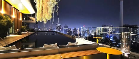 A rooftop terrace with a pool, seating areas, and a city skyline view.