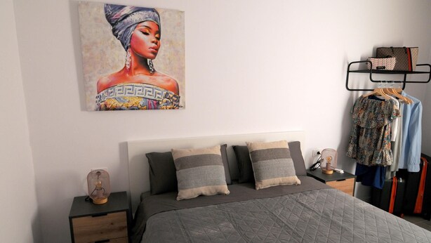 Un dormitorio con cama, una mesita de noche, un estante con ropa y un cuadro.