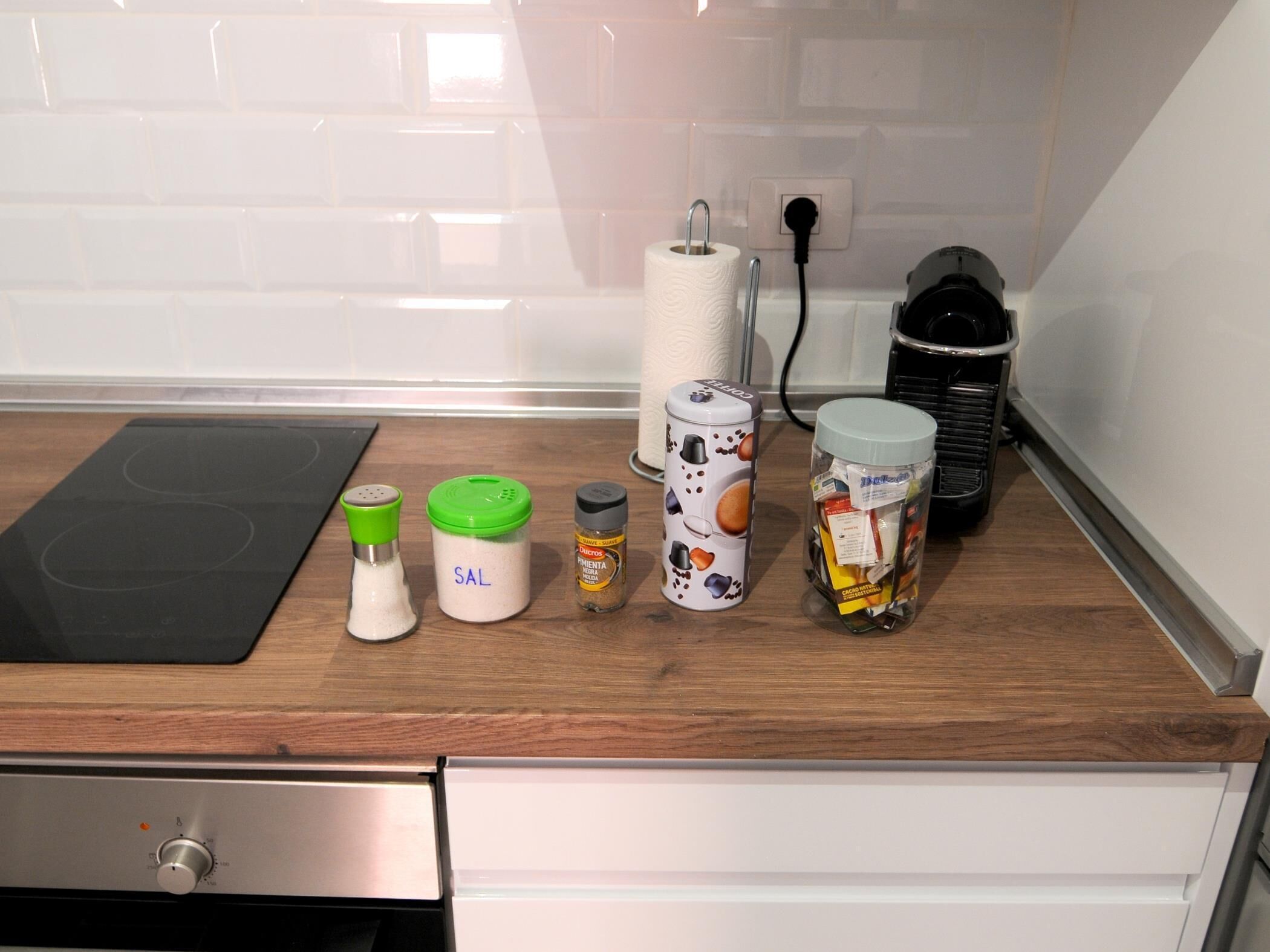 A kitchen counter with a black induction cooktop, a white paper towel holder, a salt shaker, a pepper shaker, a jar of spices, and a jar of pasta sauce.
