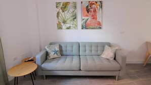 Un salón con un sofá gris, dos cojines, una mesita de madera y dos cuadros colgados en la pared.