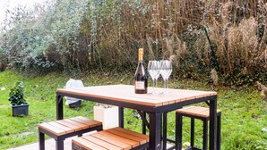 Une table en bois installée à l’extérieur, avec des bancs, une bouteille de vin et deux verres, le tout sur une terrasse.