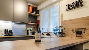 Un comptoir de cuisine avec une bouteille de vin et des verres, une machine à café et une enseigne de bar.