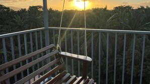Un banco de madera en un balcón con vista al atardecer sobre un área boscosa.