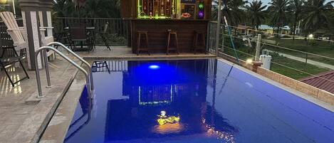 A swimming pool with a bar area, a neon sign, and outdoor seating.